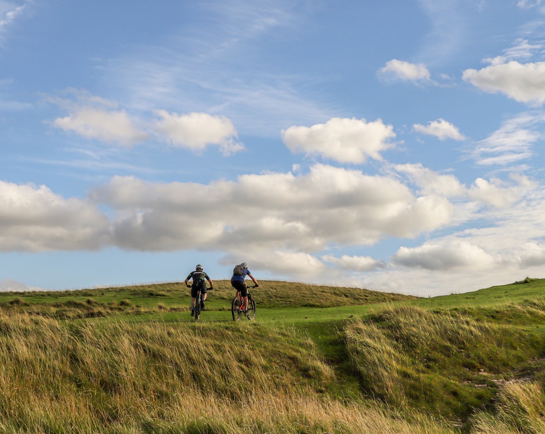 Two cyclists riding on a grassy hill under dramatic clouds